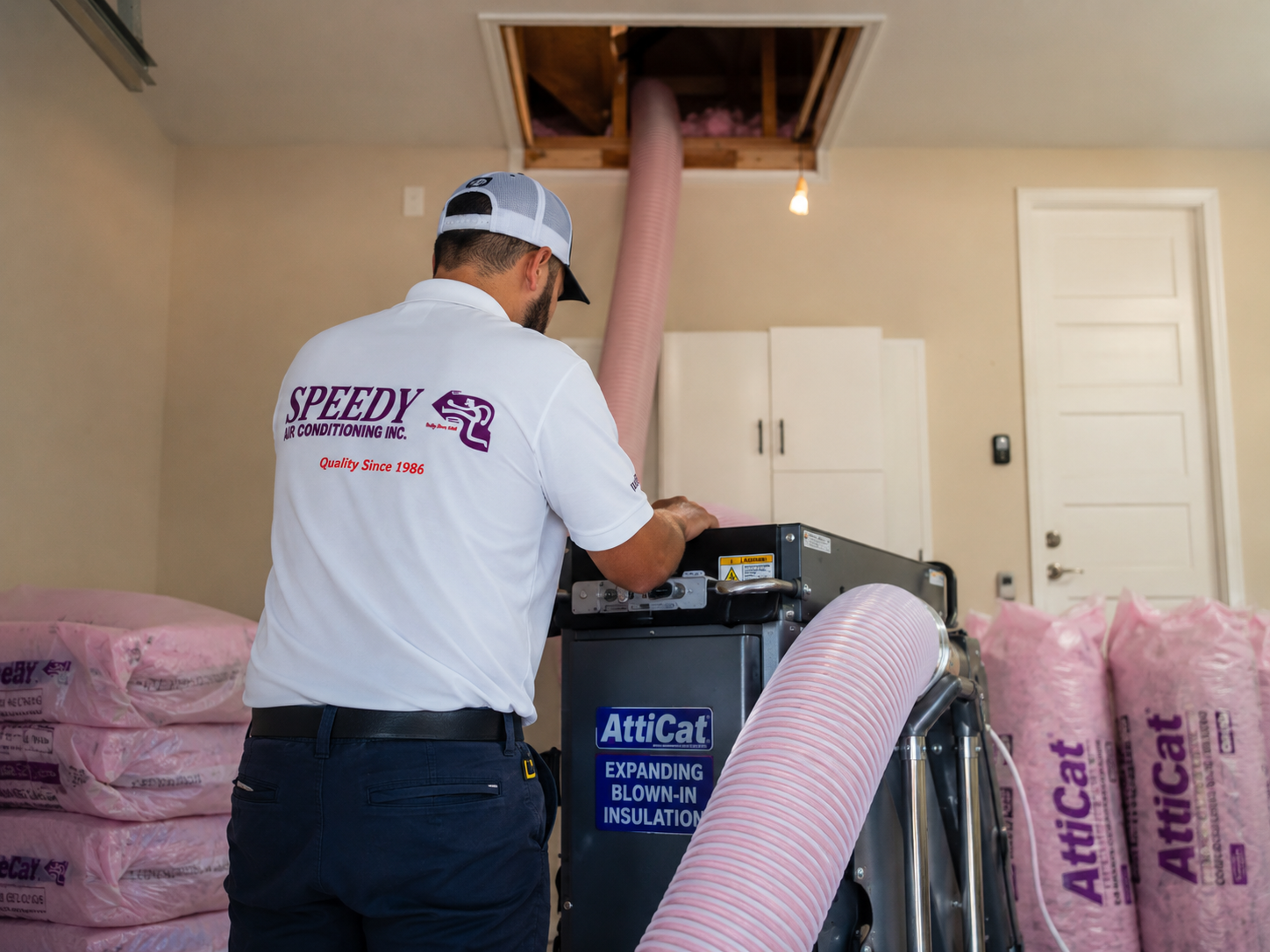 Speedy technician operating an Owens Corning AttiCat blown-in insulation machine in a Naples garage.