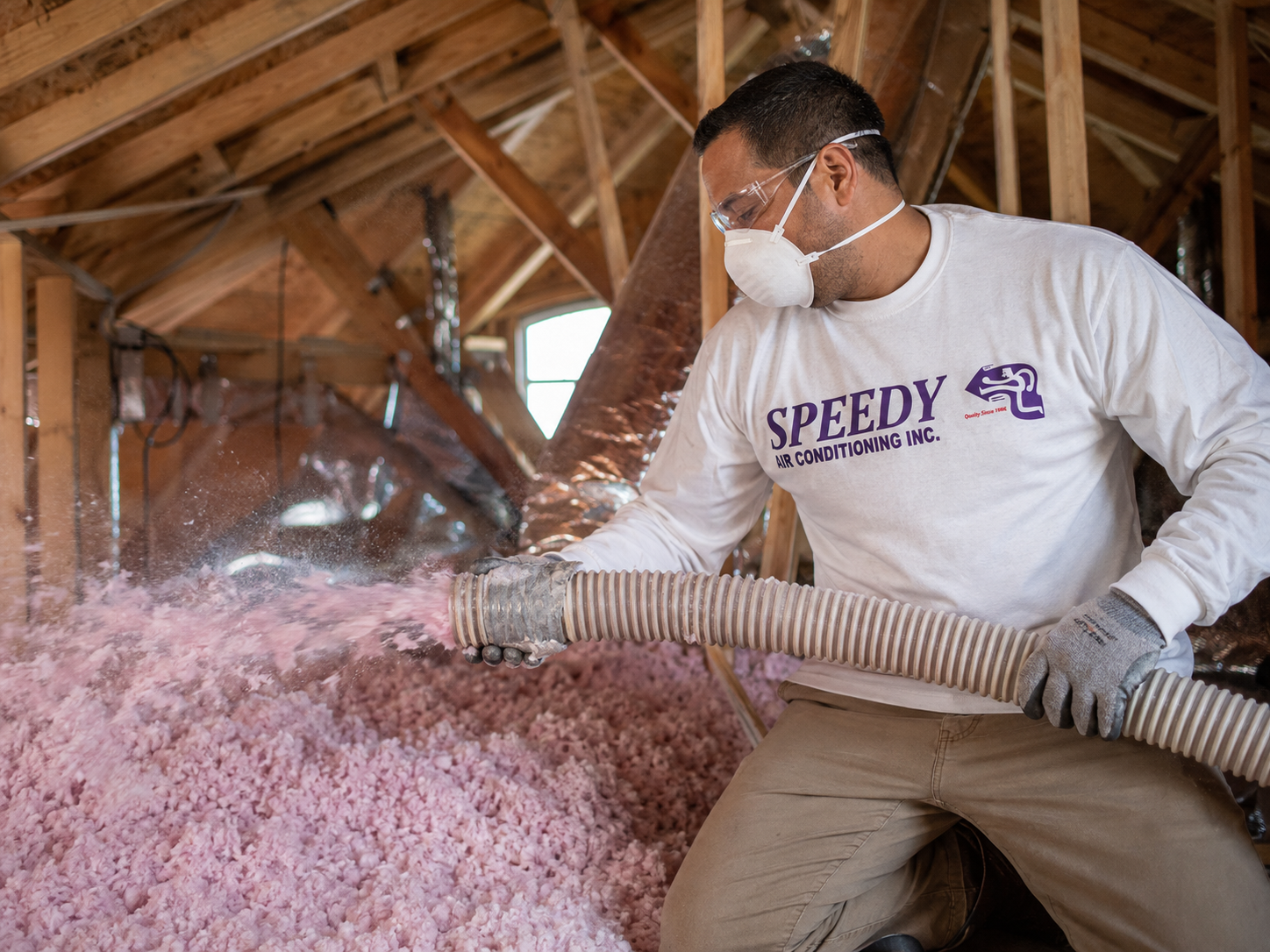 Speedy technician blowing pink Owens Corning insulation evenly across an attic floor.